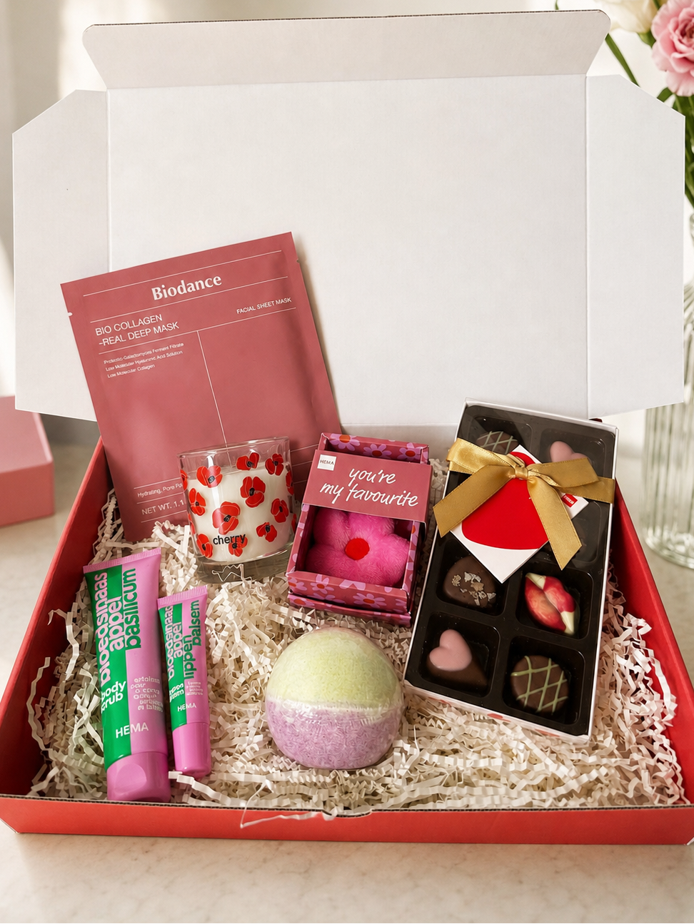 Gift box with skincare products, candles, and chocolates on a white surface.